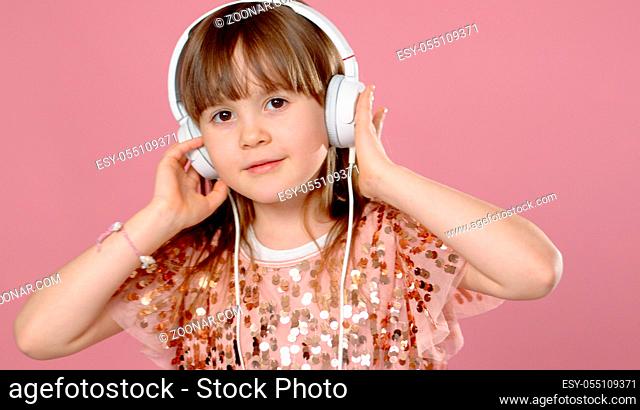 Cute little girl posing and dancing with headphones while listen to the music. Standing isolated on pink background with copyspace
