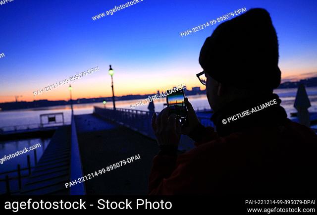 14 December 2022, Hamburg: A man takes a photo with his smartphone at the Rabenstraße jetty on the Alster before sunrise