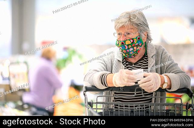 27 April 2020, Baden-Wuerttemberg, Leinfelden-Echterdingen: A customer with a colourful mouthguard sewn by her daughter is shopping at Edeka Bauer