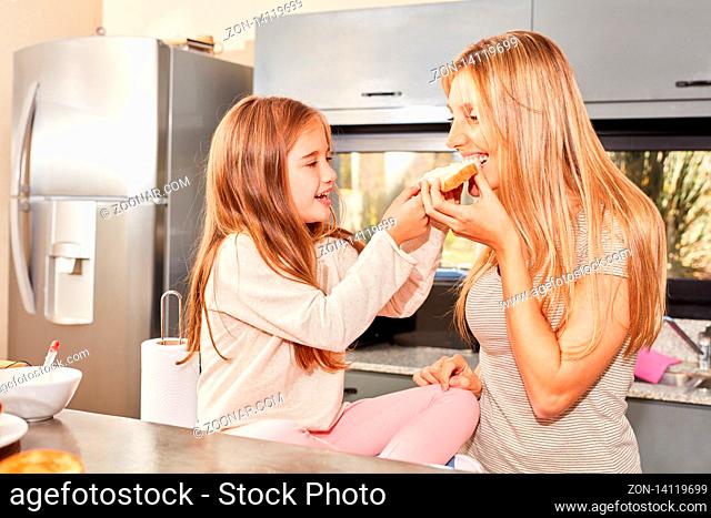 Mutter wird von ihrer Tochter mit Toast Brot gefüttert beim Frühstück in der Küche