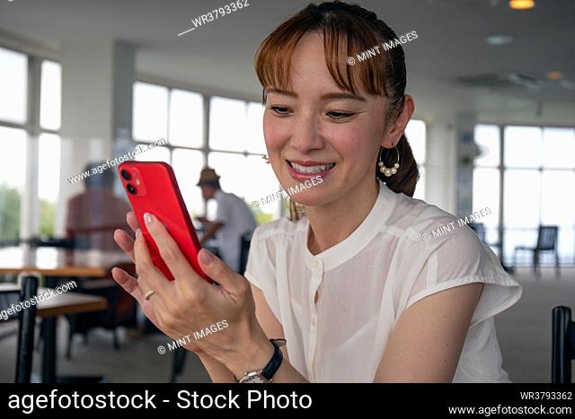 A mature Japanese woman looking at her phone screen and smiling, sending a text, messaging