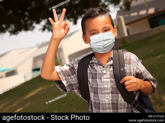 Hispanic student boy wearing face mask with backpack on school campus