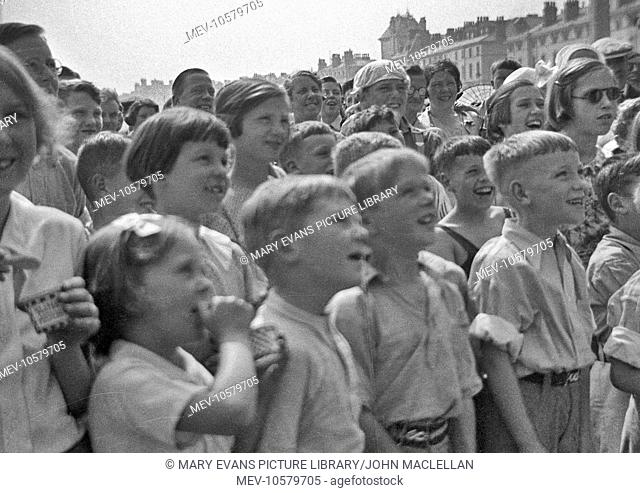 Children's entertainment on a beach -- they are probably watching a Punch and Judy show