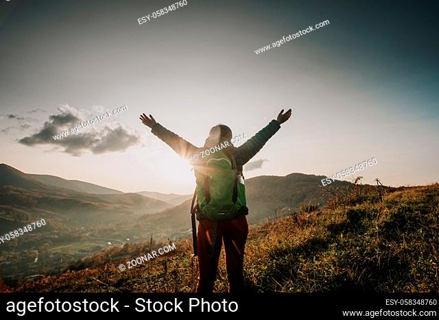 Woman with a backpack standing on the mountain slope with widely opened arms. Woman enjoying the moment of uniting with nature