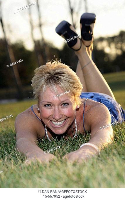 Middle aged blond woman dressed up playfully on the grass to enjoy the sunset or sunrise