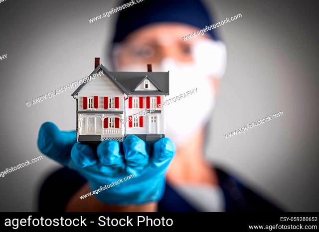 Female Doctor or Nurse Wearing Surgical Gloves Holding Model Home