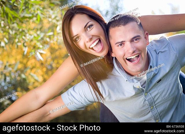 Happy mixed-race romantic couple piggyback portrait in the park