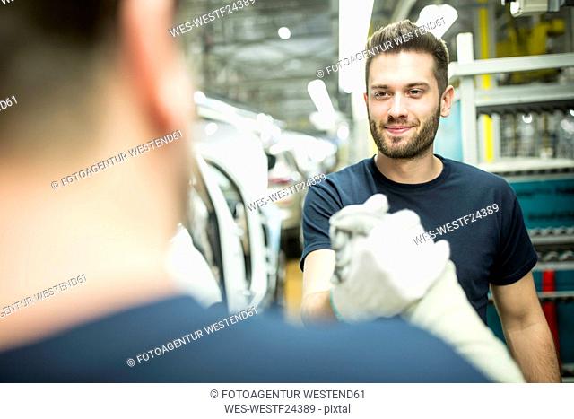 Two colleagues shaking hands in modern car factory