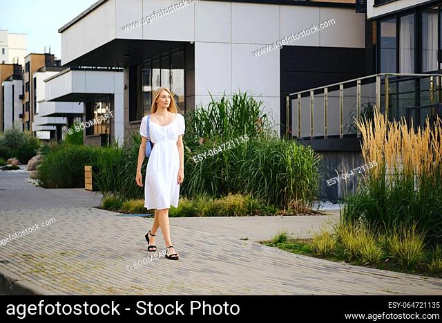Blonde woman walking along the pavement in modern residential area