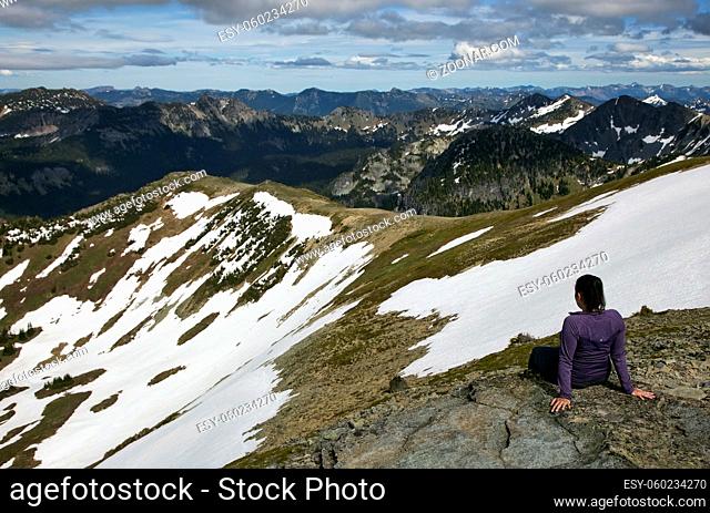 A female hiker stops to rest and enjoy the view at the top of a partially snowy mountain