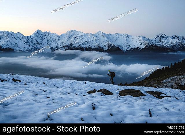 Man with hiking poles walking in the snow with majestic Orobie Alps in the background, Alpe Rogneda, Rhaetian Alps, Lombardy, Italy, Europe