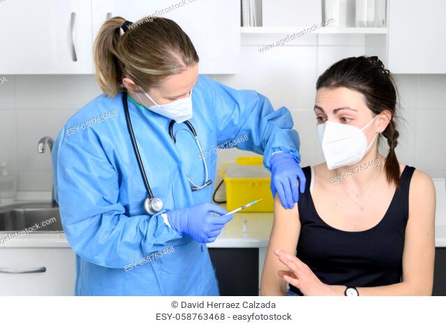 Young woman in face mask scared of coronavirus vaccine, not letting doctor make injection at clinic. Woman afraid of covid-19 vaccination