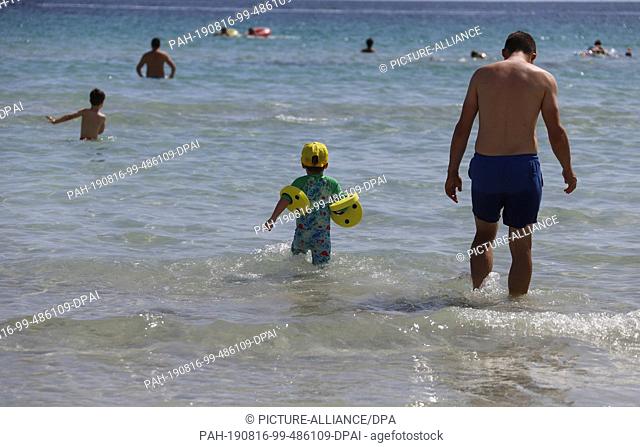 14 August 2019, Spain, Alcudia: Swimmers stand in the light swell. Photo: Clara Margais/dpa. - Alcudia/Mallorca/Spain
