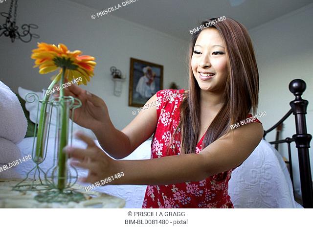 Smiling mixed race teenage girl placing flowers in vases on bedside table