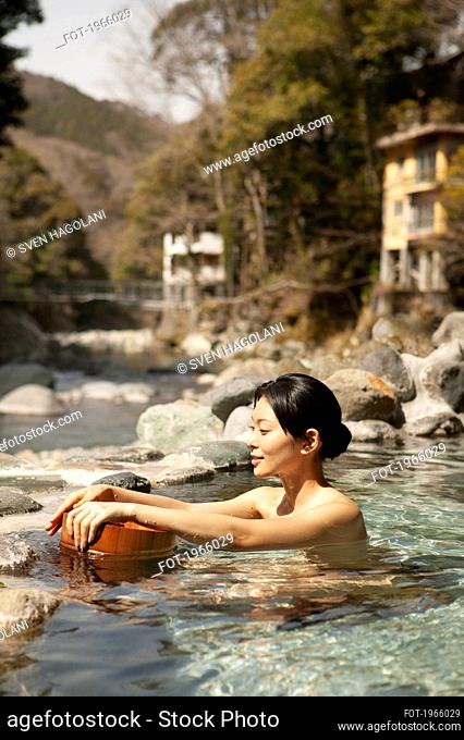 Young woman with bucket in sunny pool at Onsen
