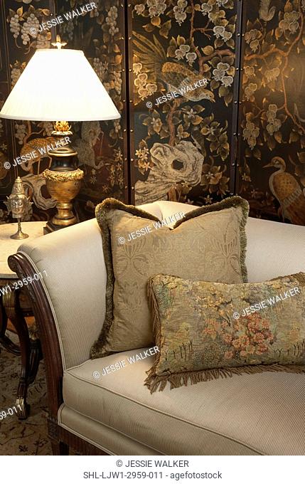 Living room detail of end of sofa with two large pillows, end table with accessories including Buddah head, lamp with ornate base, sitting area, reading area