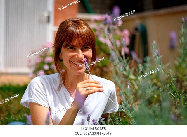 Mid adult woman sitting smelling lavender, smiling at camera