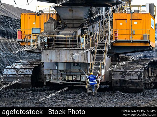 PRODUCTION - 19 December 2023, Brandenburg, Jänschwalde: An employee of Lausitz Energie Bergbau AG (LEAG) climbs onto a huge mining machine at the coal seam in...