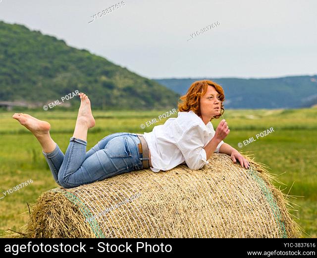 Mature woman laying down on haystack serious looking away