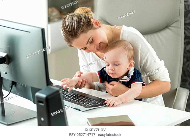 Young smiling woman working at home and holding her baby son on lap