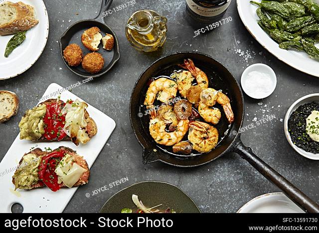 King prawns in a pan with garlic and parsley alongside several other dishes on the table