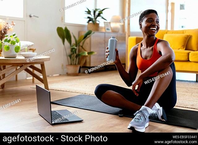 Happy woman sitting with water bottle at home
