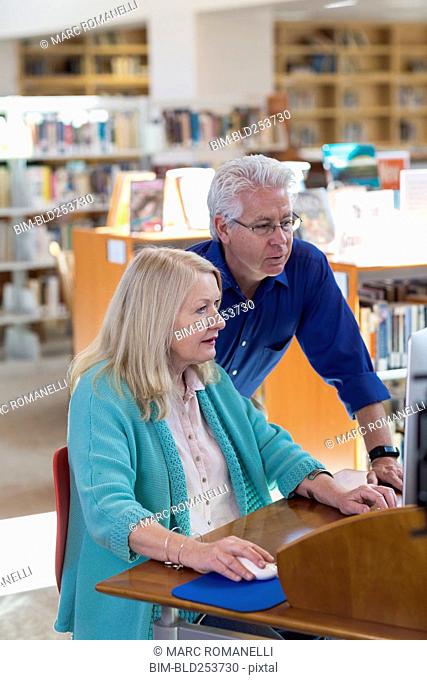 Older man helping woman using computer in library