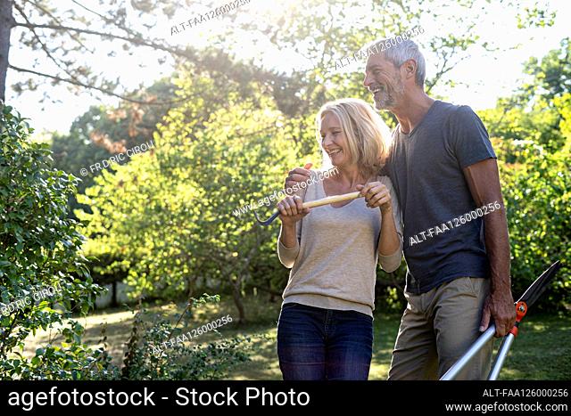 Cheerful mature couple with gardening equipment standing in backyard