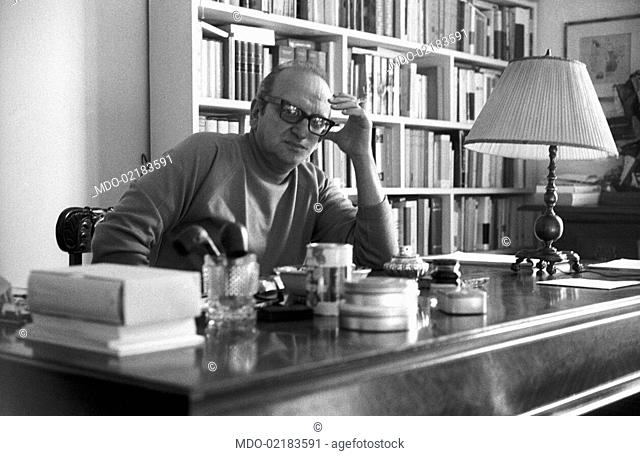 Italian writer Vasco Pratolini sitting at his desk at home. Rome, 1969