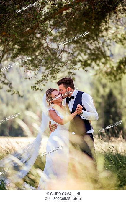 Romantic groom kissing bride on cheek in woodland
