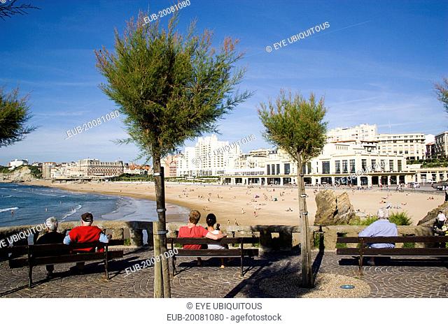 The Basque seaside resort on the Atlantic coast. Tourists sitting on benches beneath tamarisk trees overlooking the Grande Plage beach with the Casino Municipal...