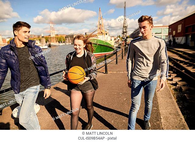 Three friends walking beside river, young woman carrying basketball, Bristol, UK