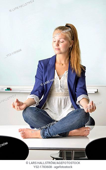 Attractive businesswoman sitting barefoot in yoga position on a table in her workplace