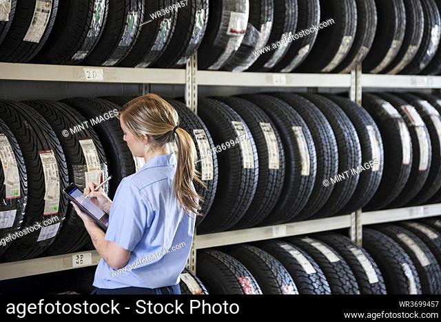 Young female mechanic takes inventory of new tires in repair shop