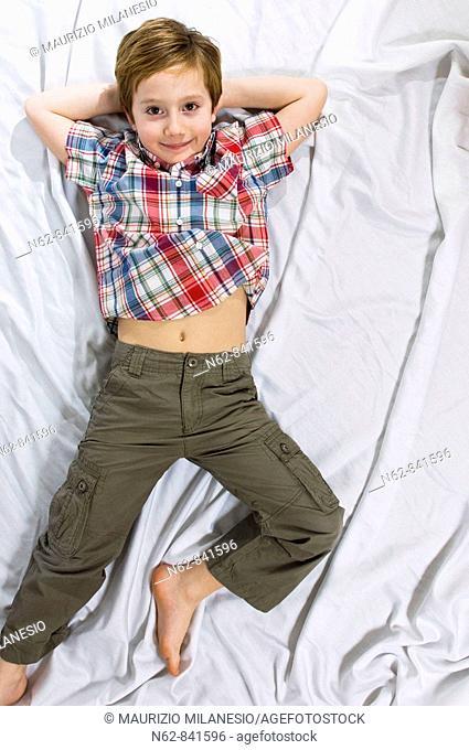 smiling baby lying on the bed with his arms behind his head