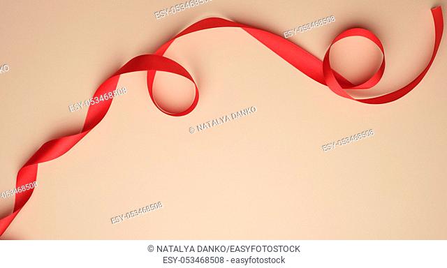 red silk ribbon twisted on a beige background, festive backdrop, copy space