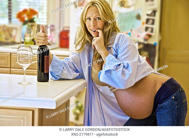 Pregnant woman is tempted by wine in her kitchen