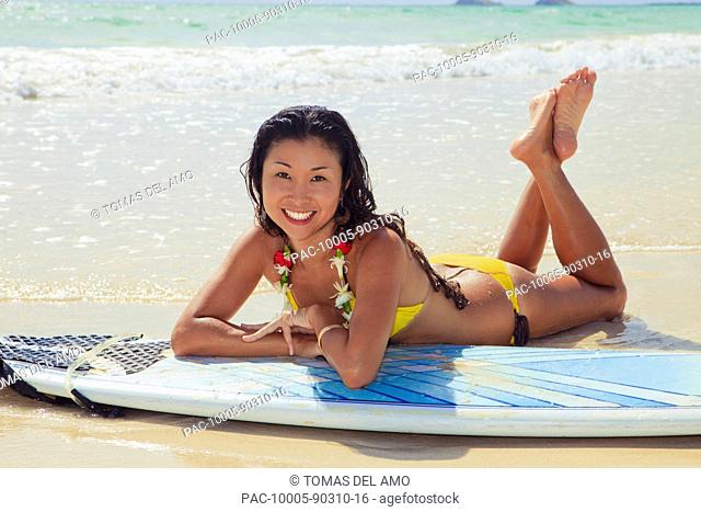 Hawaii, Oahu, Young woman poses with her surfboard on beach