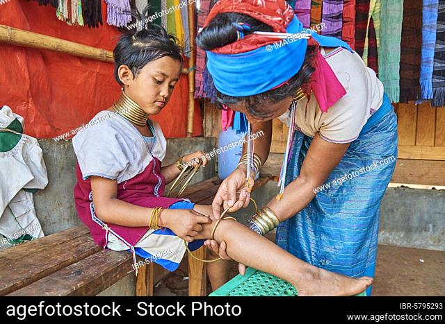 Kayan Lahwi woman putting a brass coil on the lower leg of her daughter, Pan Pet Region, Kayah State, Myanmar, Asia