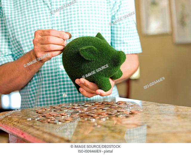 Man putting coins in green piggy bank