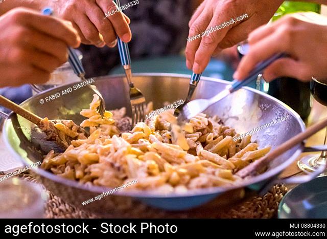 close up with different many hands friends taking italian pasta together with the forks to have fun and enjoy the friendship