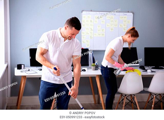 Two Smiling Young Janitor Cleaning The Desk And Mopping Floor In The Office