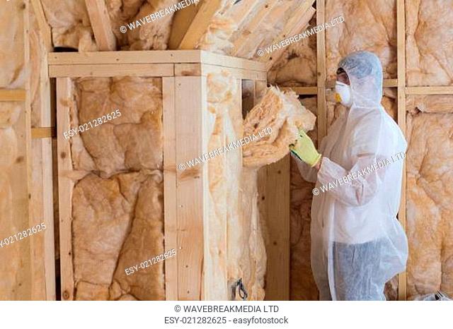 Worker filling walls with insulation material in construction site