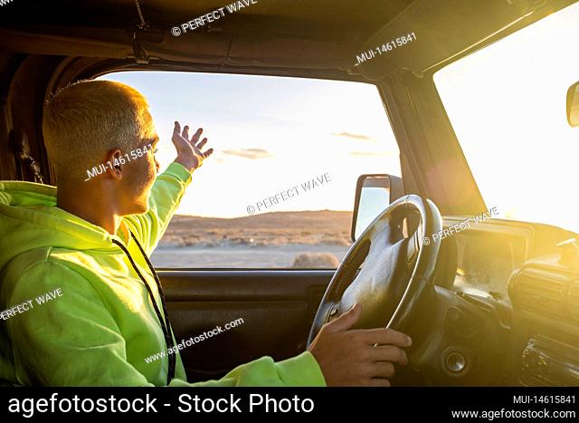 one young man driving his car and looking at the sunset enjoying his vacations and holiday outdoor alone - travelling and journey concept - teenager with car...