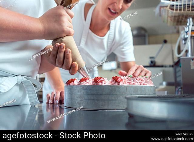 Confectioner or pastry chefs finishing cake with pastry bag, close-up on hands