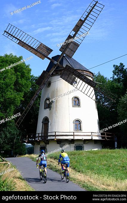 26 July 2023, Saxony, Dresden: Cyclists pass the Gohlis windmill on the Elbe cycle path in the morning. The mill was built from 1828 to 1832