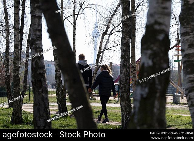 25 March 2020, Berlin: A couple walks holding hands in sunny weather through the small birch grove in Mauerpark. Photo: Jörg Carstensen/dpa