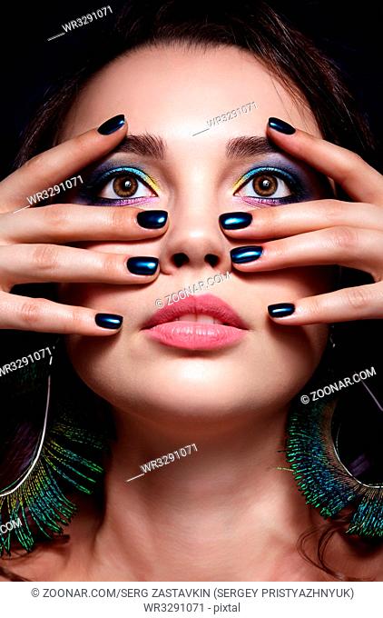Portrait of beautiful brunette woman on black background. Female with blue eye shadow make up and manicure. Girl with peacock feather earrings
