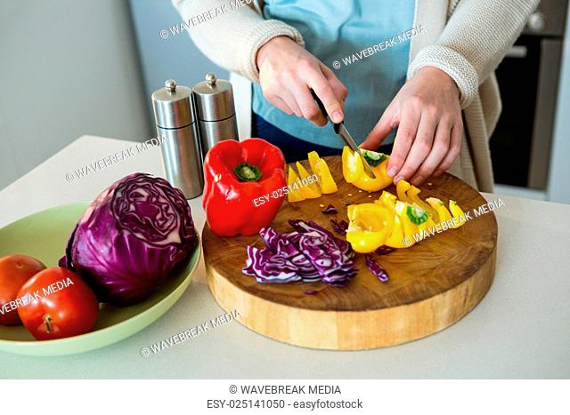 Mid section of woman cutting yellow bell pepper in kitchen