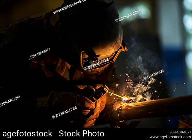 Welder at work. Man in a protective mask. The welder makes seams on the metal. Sparks and smoke when welding
